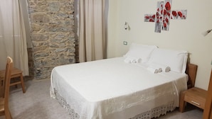 Un dormitorio con pared de piedra, una cama con ropa blanca, una mesita de noche de madera y una silla.