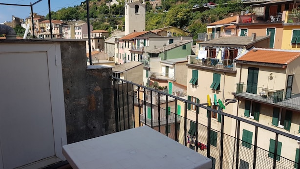 Un balcón con una mesa blanca, con vistas a una zona residencial con edificios de colores y una torre de iglesia.