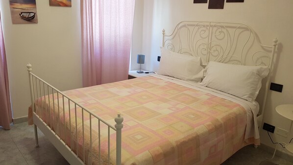 A neatly made bed with a patterned bedspread, a white metal headboard, and a bedside table with a lamp. - Vento di grecale (Riomaggiore)