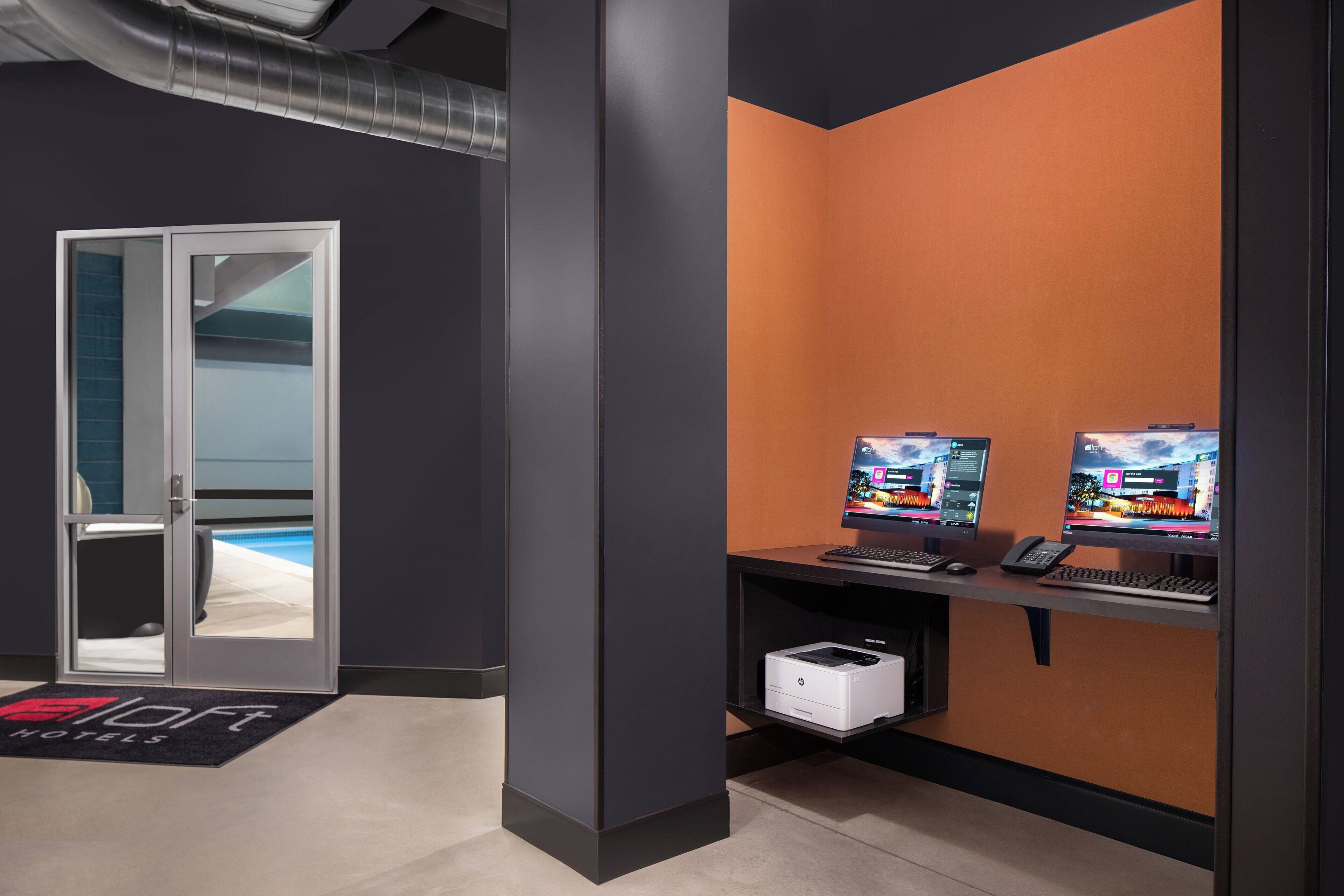 Ein Hotel-Empfangsbereich mit einem Schreibtisch, zwei Monitoren, einem Drucker und einer Tür zum Pool.