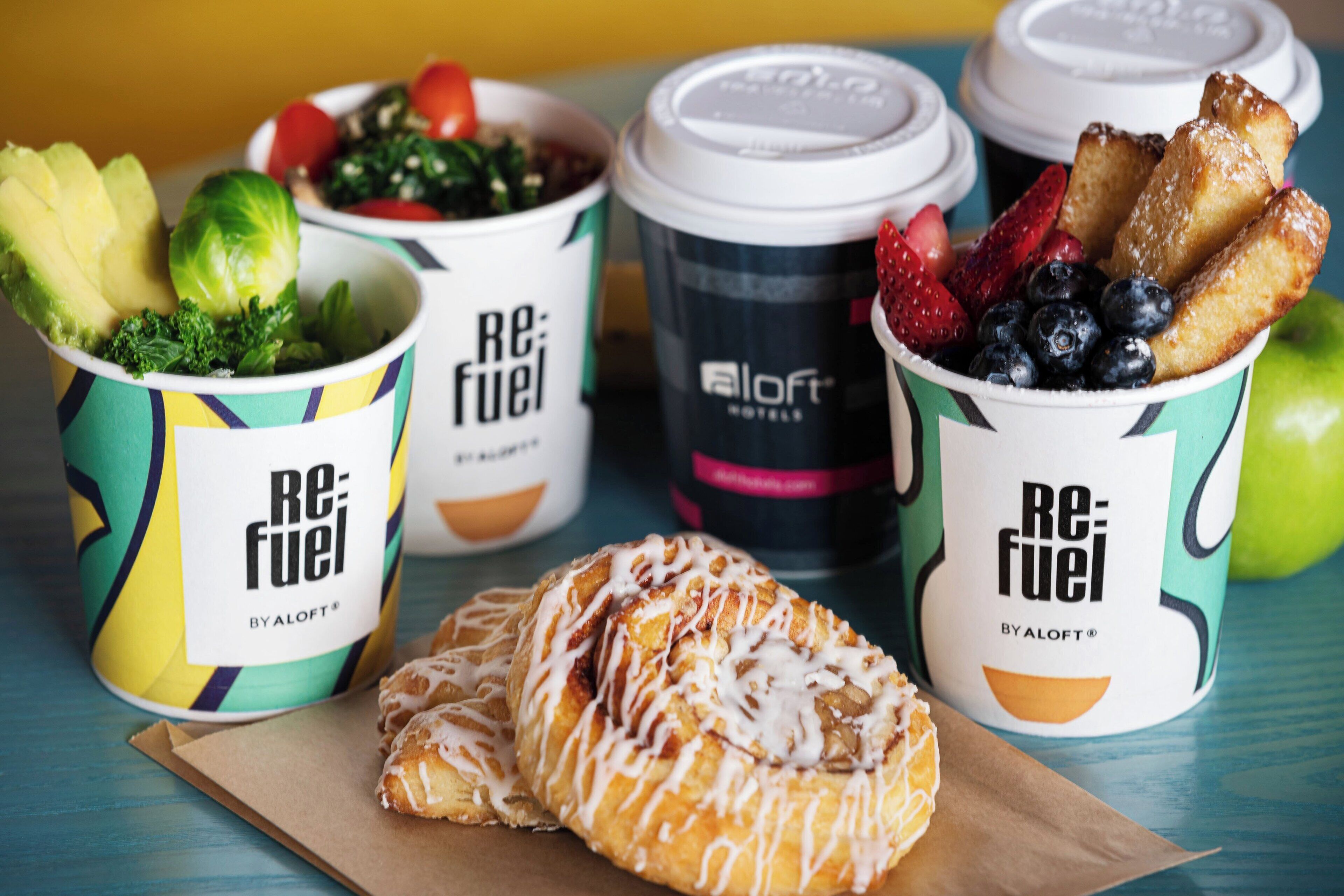 A table with food items and coffee cups labeled 'Re:Fuel' by Aloft Hotels.