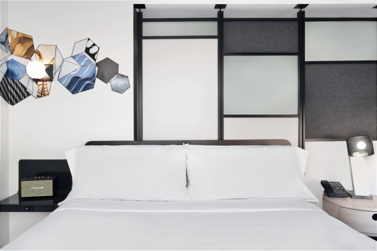 A hotel room with a bed, a nightstand with a radio, a lamp, and a phone.