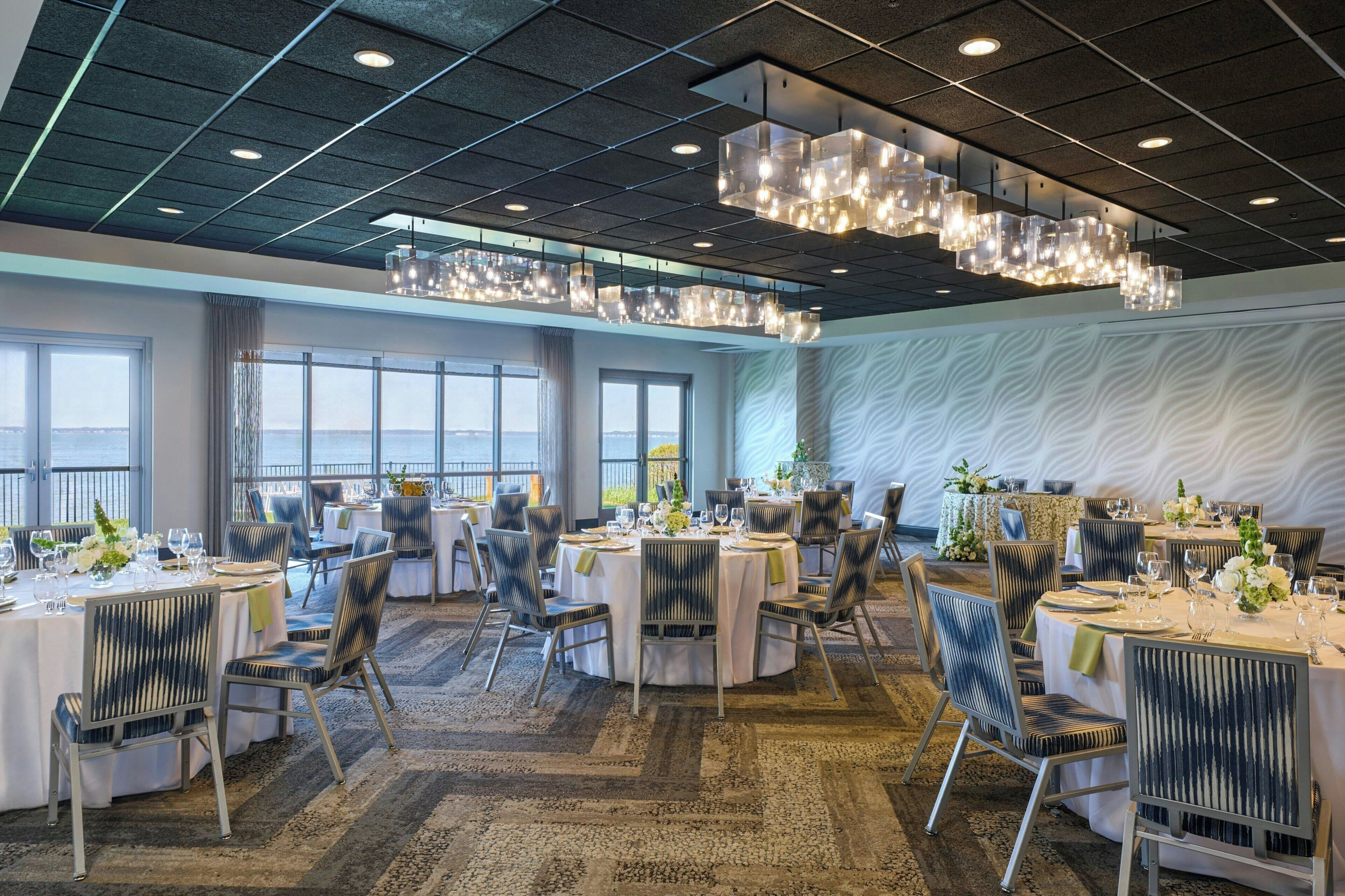 A spacious dining area with round tables, chairs, and a modern chandelier.