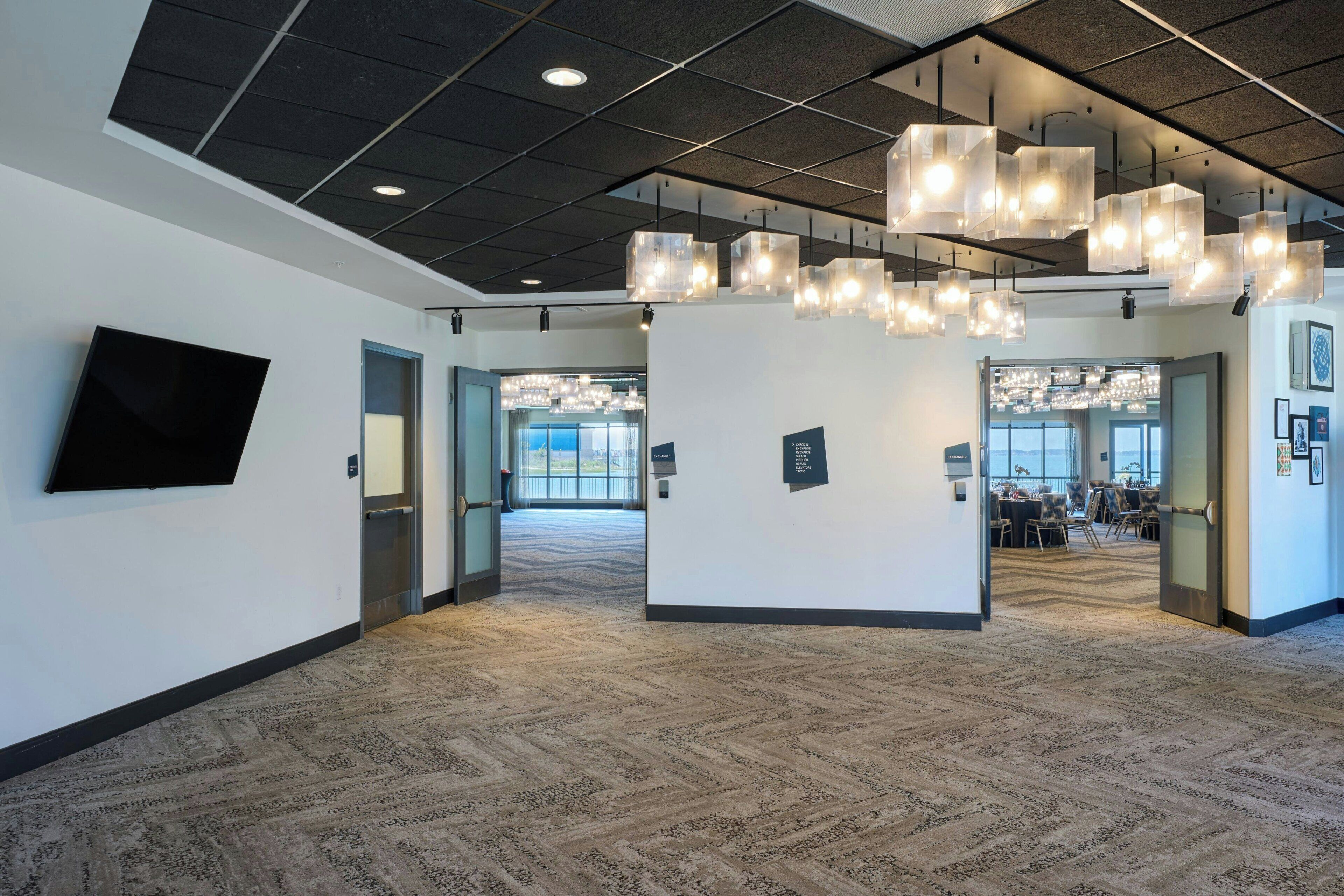 A spacious lobby with patterned carpet, a flat-screen TV, and multiple hanging lights.