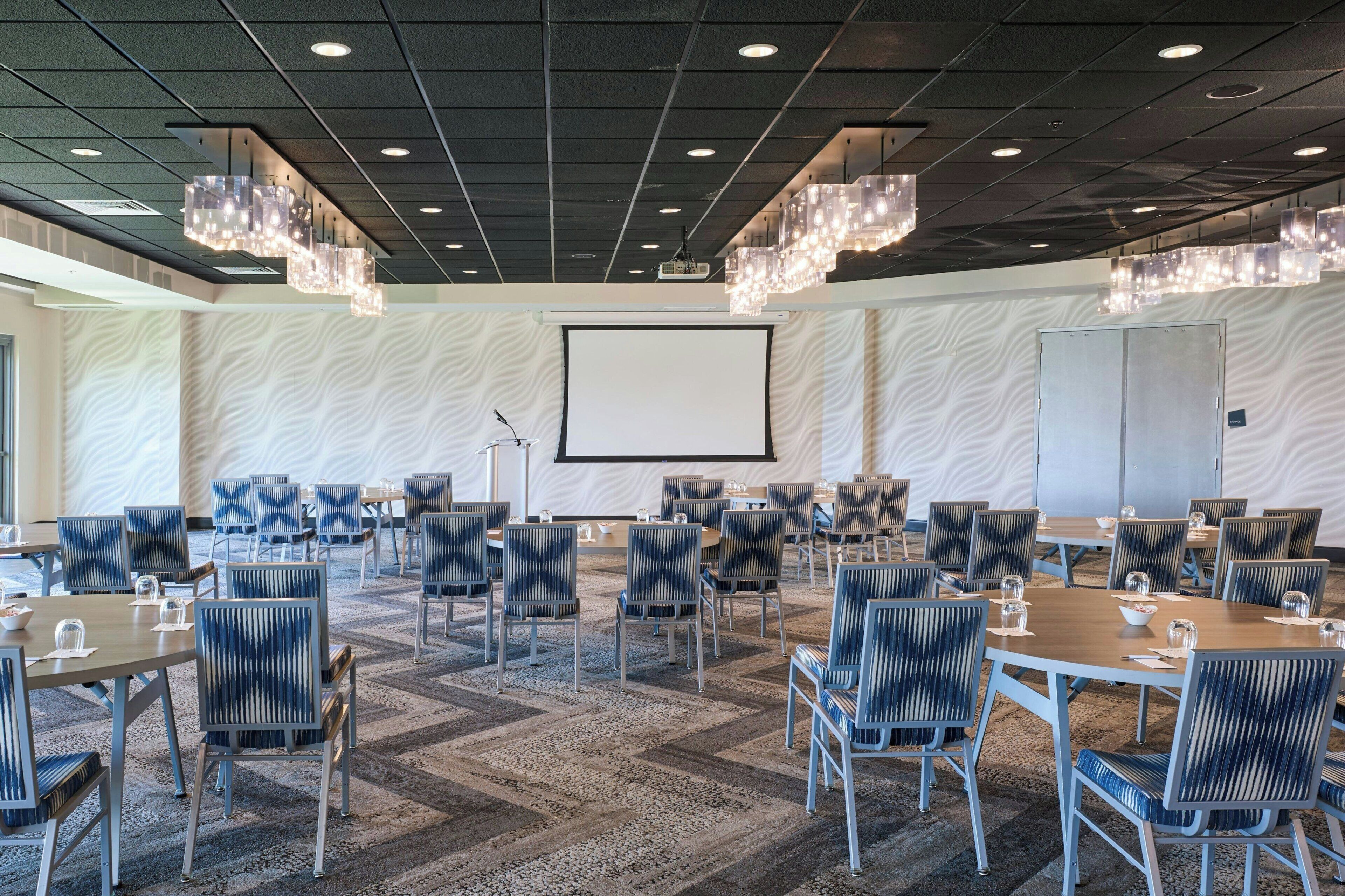 A conference room with a large screen, multiple tables, and chairs arranged for meetings.