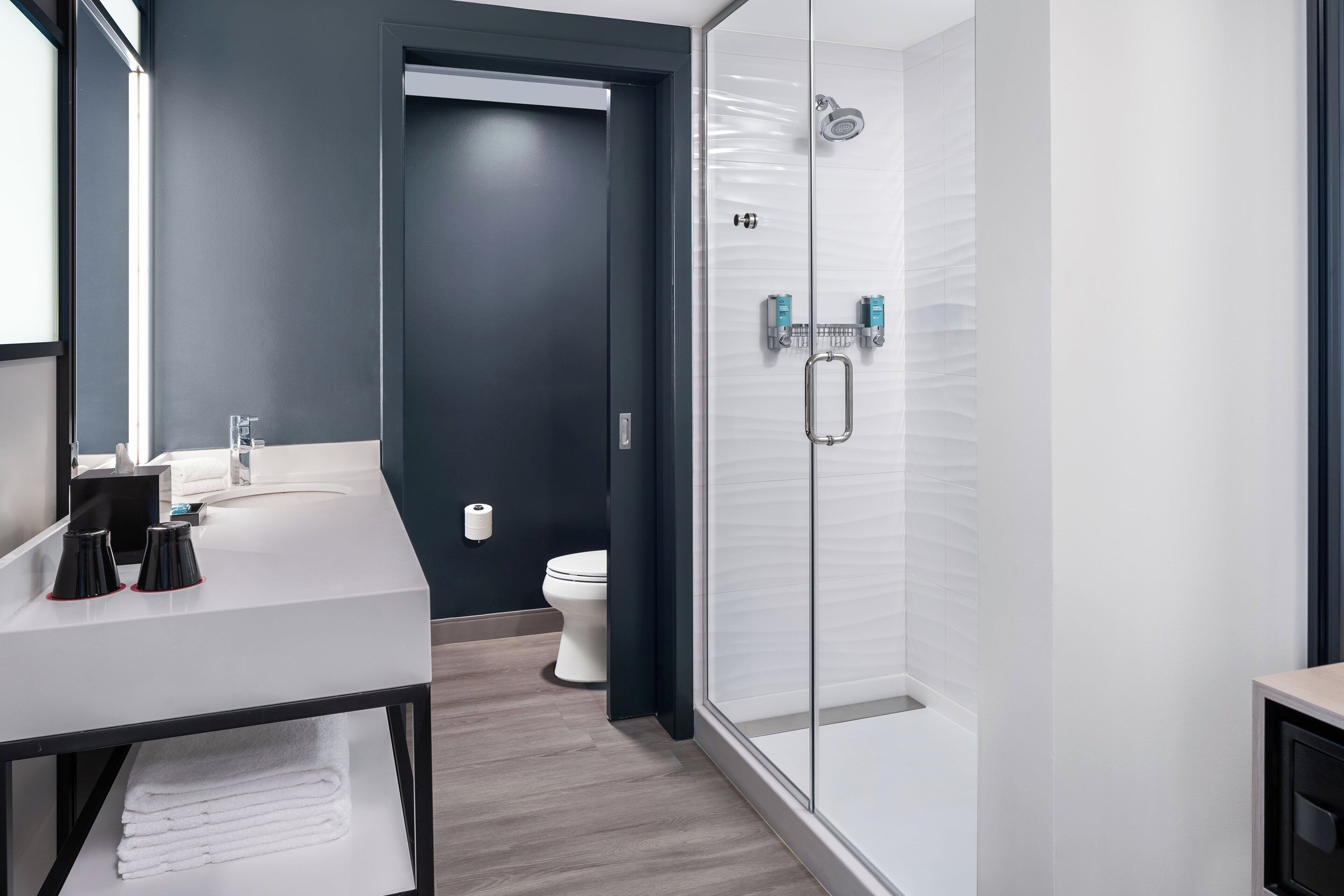 A modern bathroom with a glass shower enclosure, a white sink, and a dark wall.