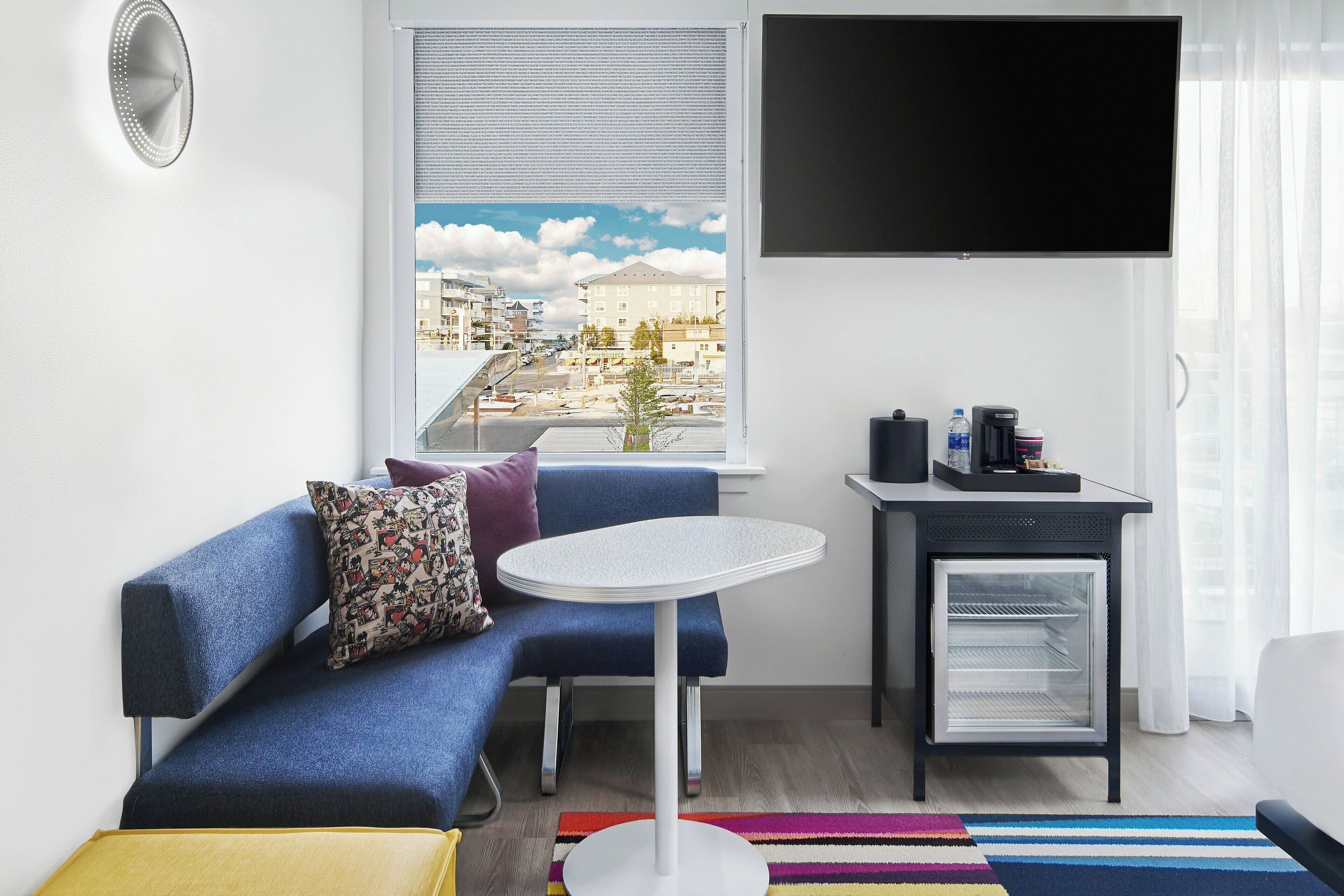 Un salon moderne avec un canapé bleu, une petite table ronde, un mini-réfrigérateur et un téléviseur fixé au mur.