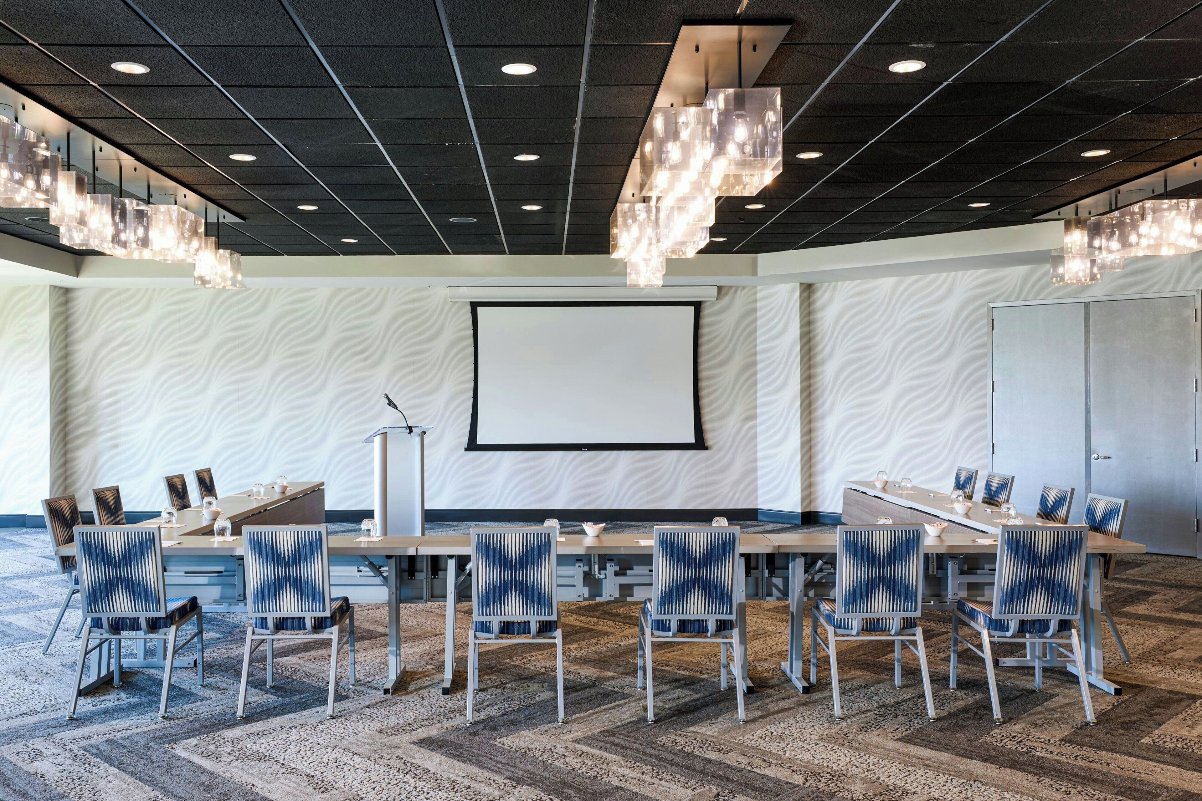 Un salón de conferencias con una gran mesa, sillas, una pantalla de proyector y un papel tapiz con diseño.