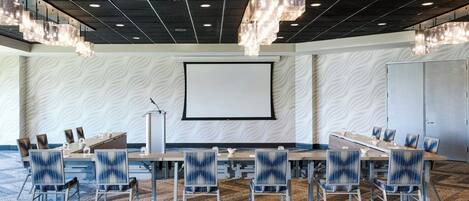 Un salón de conferencias con una gran mesa, sillas, una pantalla de proyector y un papel tapiz con diseño.