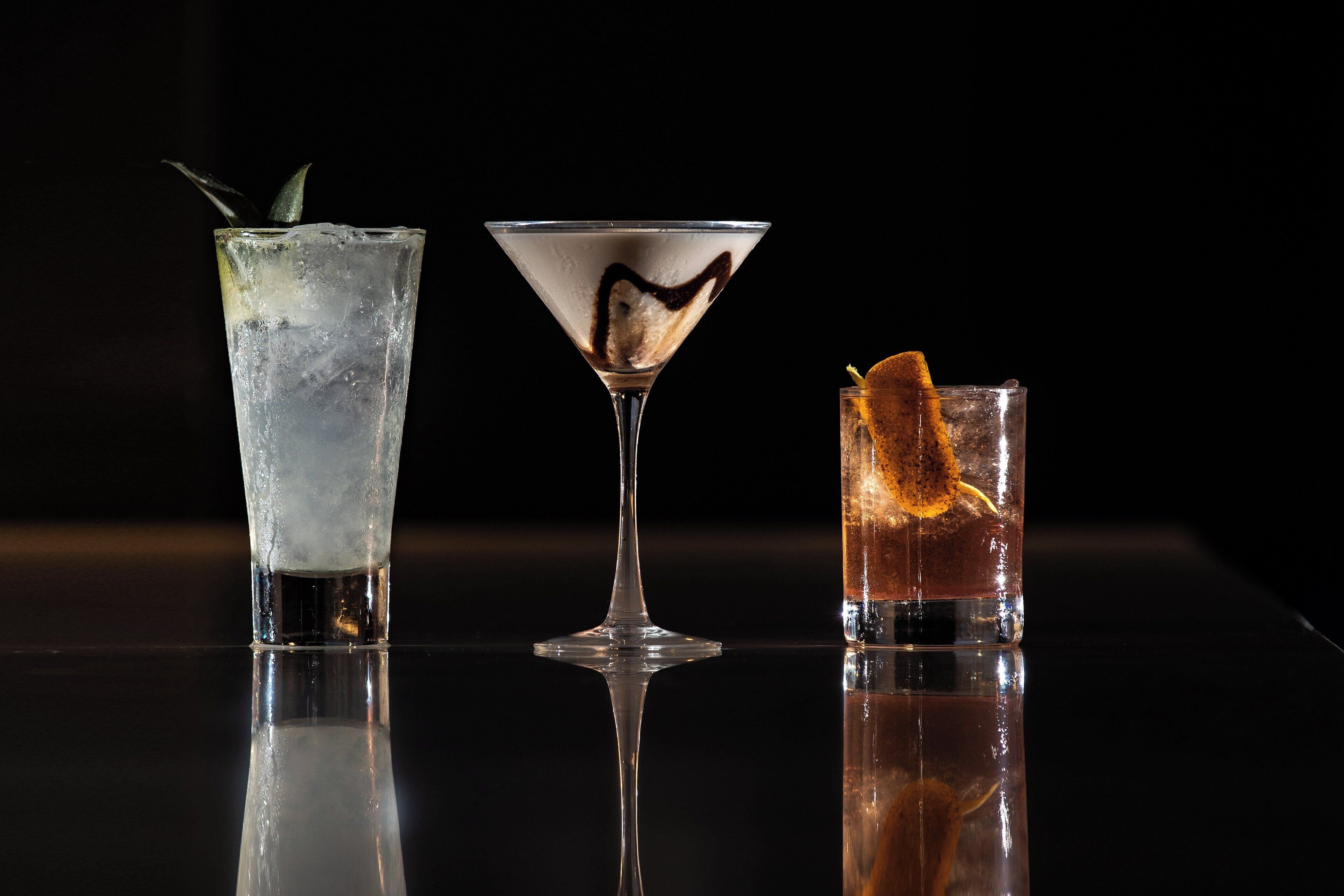 Three glasses of different beverages on a reflective surface.