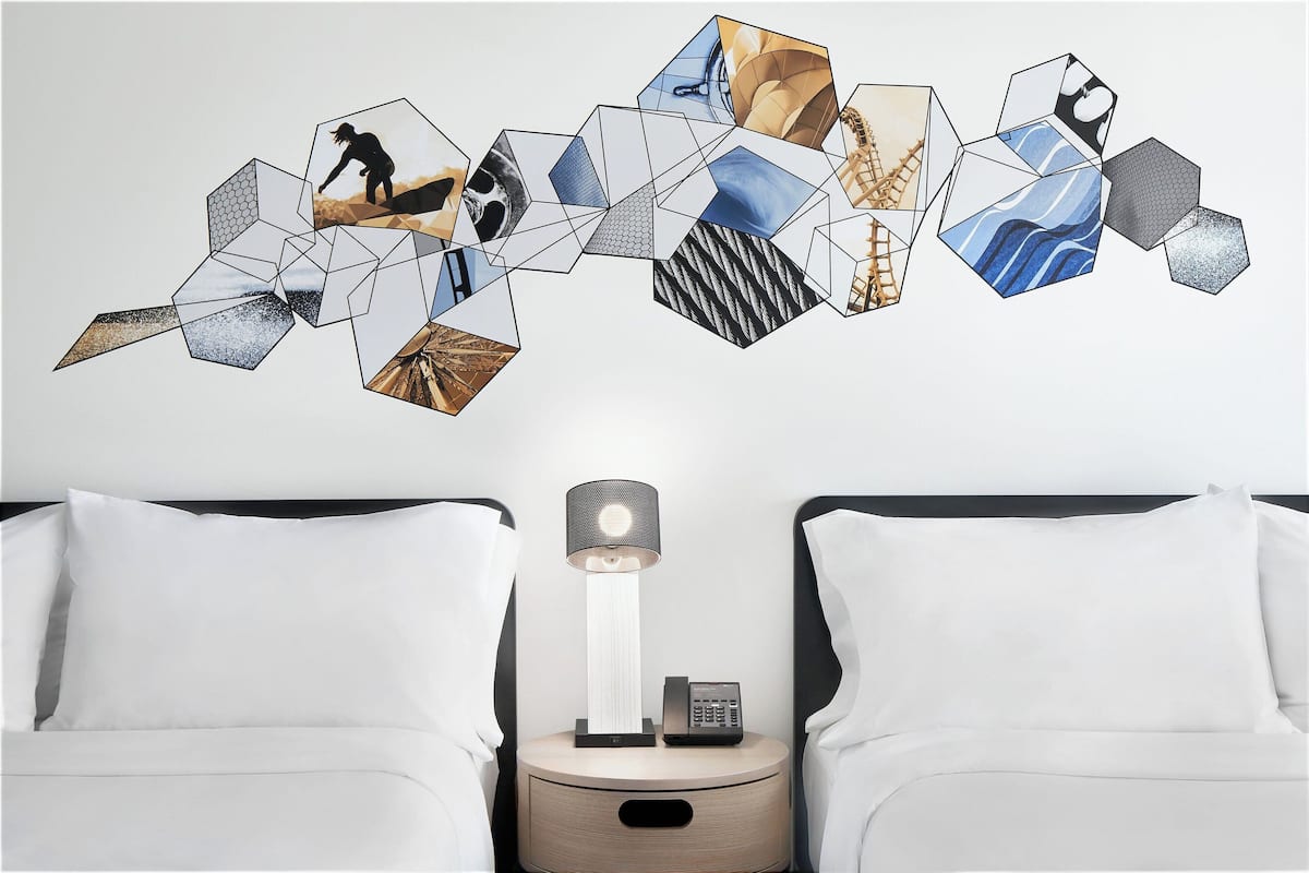 A bedroom with two beds, a bedside table with a lamp and phone, and a wall decoration of hexagonal shapes.