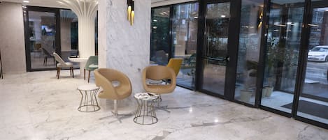 A modern lobby with marble flooring, contemporary chairs, and large glass doors leading outside.