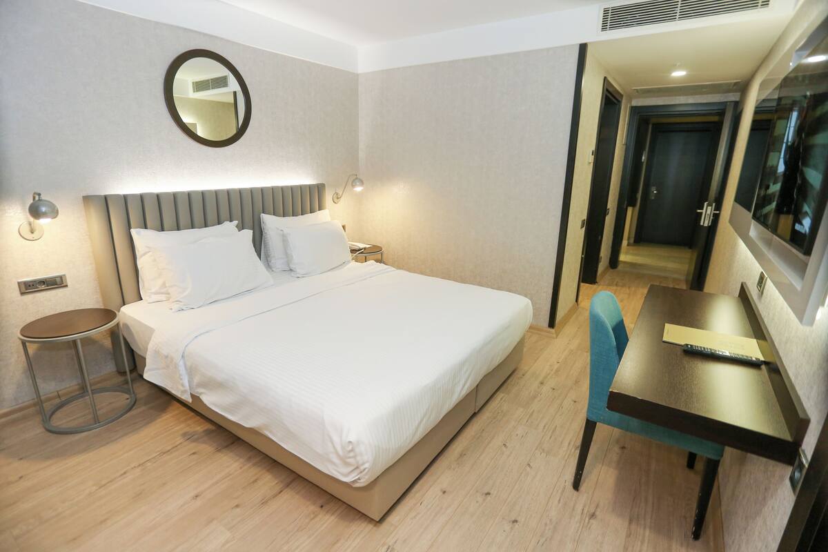 Ein Hotelzimmer mit einem Bett, einem Nachttisch, einer Lampe und einem Schreibtisch mit Stuhl.