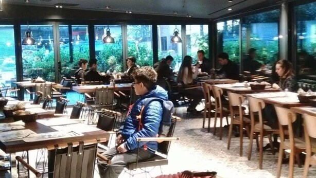 A restaurant with multiple tables and chairs, a buffet with various food items, and large windows offering a view of the outdoors. - Milord Hotel (Istanbul)