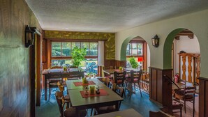 A dining area with wooden tables and chairs, large windows with views of greenery, and a staircase with wooden railings. - Mühlen Hotel Konschake (Burgen)