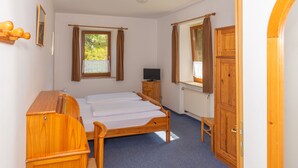 A bedroom with a wooden bed, a small wooden dresser, a television, and a window with curtains. - Mühlen Hotel Konschake (Burgen)