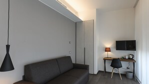 A modern room with a grey sofa, a desk with a chair, a lamp, and a TV on the wall. - B&B The Attico (Florence)