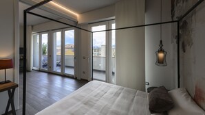 A bedroom with a large bed, a desk with a lamp, and a balcony with a view of buildings. - B&B The Attico (Florence)