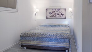 Una habitación pequeña con una cama individual, una colcha estampada, dos lámparas fijadas a la pared y un cuadro enmarcado sobre la cama.