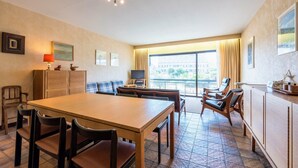 A hotel room with a dining table, chairs, a TV, a sofa, and a balcony with curtains. - Zandstuyver 102 (Koksijde)