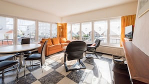 Ein modernes Wohnzimmer mit einer Couch, Sesseln, einem Esstisch und großen Fenstern mit Blick auf die Stadt.