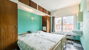 Ein Schlafzimmer mit Bett, Fenster, Nachttisch und einem Badezimmer mit Waschbecken und Spiegel.