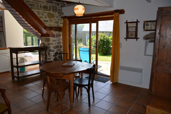 A dining area with a wooden table and chairs, a stone wall, and a view of the garden through a glass door.