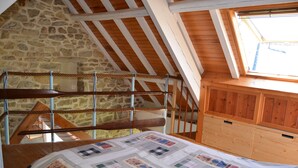 Una habitació amb sostre inclinat, bigues de fusta, paret de pedra i una finestra.