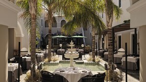 A courtyard with tables and chairs, a fountain, and palm trees.