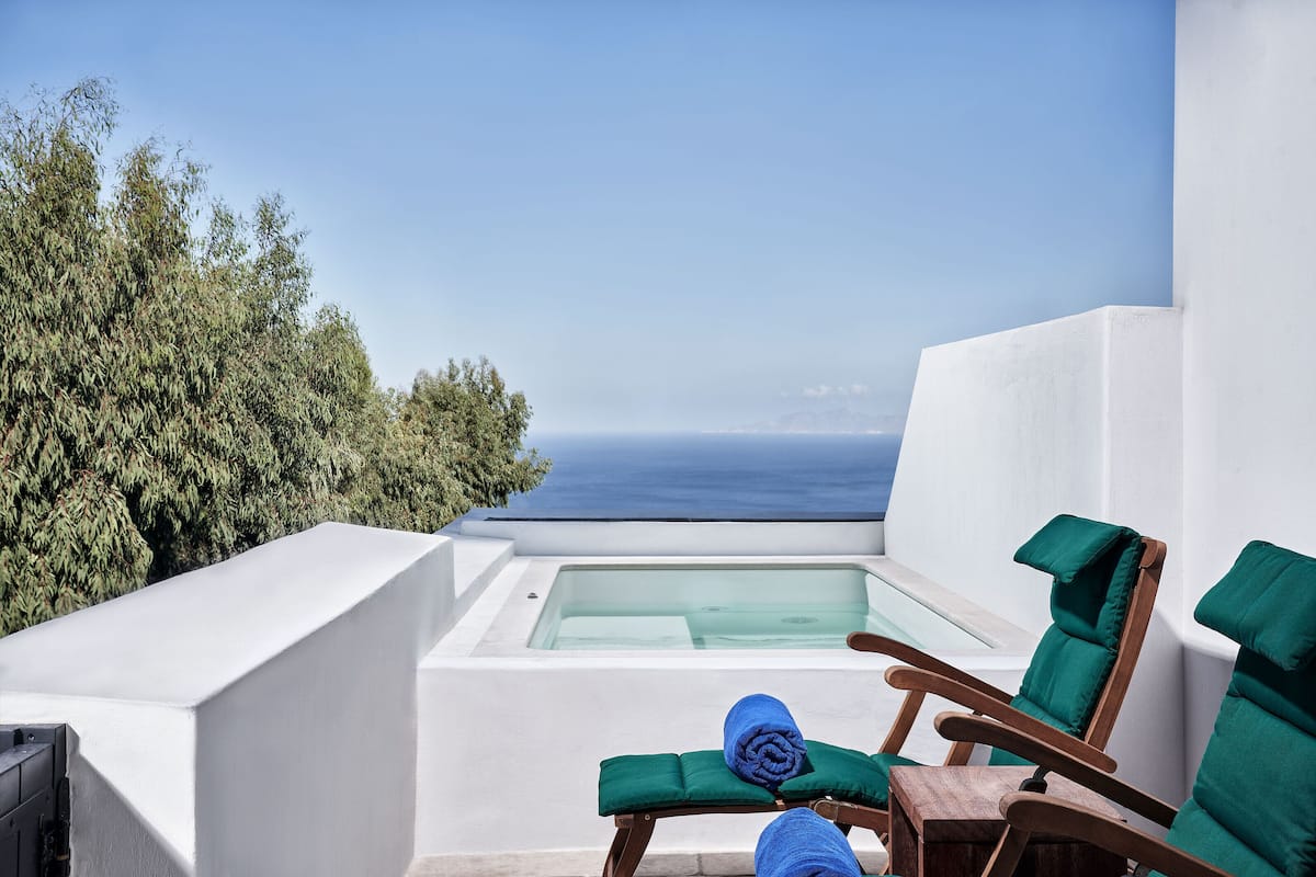 Un balcon doté d’un jacuzzi à débordement protégé par des parois en verre, de fauteuils confortables aux coussins verts et d’une vue sur la mer.