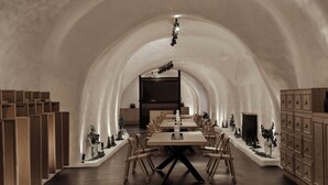 A spacious, arched interior with a long dining table and chairs, wooden cabinets, and a television.