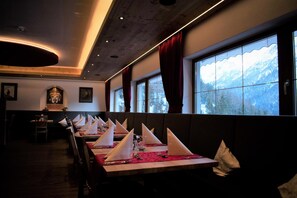 A restaurant with a long table set for a meal, large windows with a mountain view, and a modern interior design.
