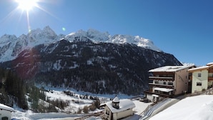Paesaggio montano innevato con un complesso turistico sciistico dotato di numerosi balconi e un tetto ricoperto di neve.