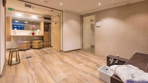 Un bagno moderno con pavimento in legno, cabina doccia in vetro e una panca con un asciugamano.