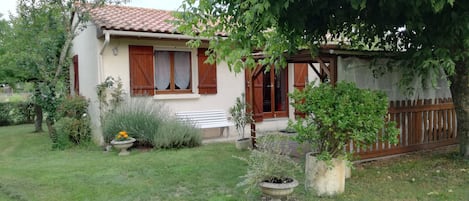 A house with a tiled roof, a wooden fence, and a garden with potted plants and a bench.