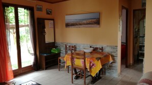 Un coin repas avec une table recouverte d’une nappe colorée, des chaises, un bol et un tableau accroché au mur.