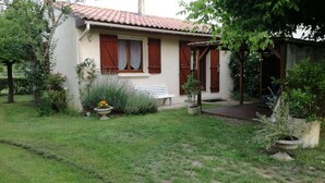 Une petite maison avec un toit en tuiles, un banc et un jardin agrémenté de plantes en pot.