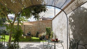 Une terrasse avec une table et des chaises, entourée d’un mur de pierre et de verdure.