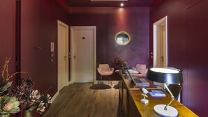 Un couloir avec un plancher en bois, un bureau avec une lampe, deux chaises et un miroir au mur.