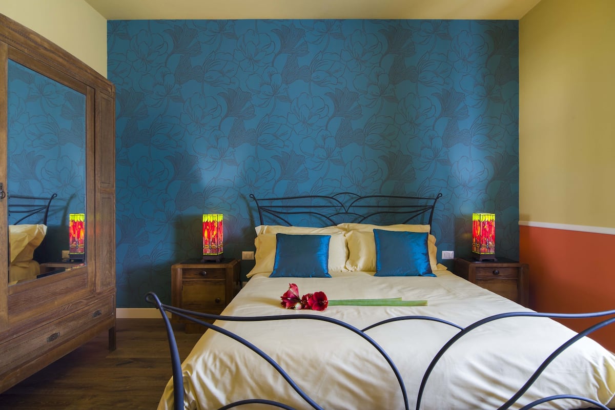 A bedroom with a large bed, two bedside tables, a mirror, and floral wallpaper.