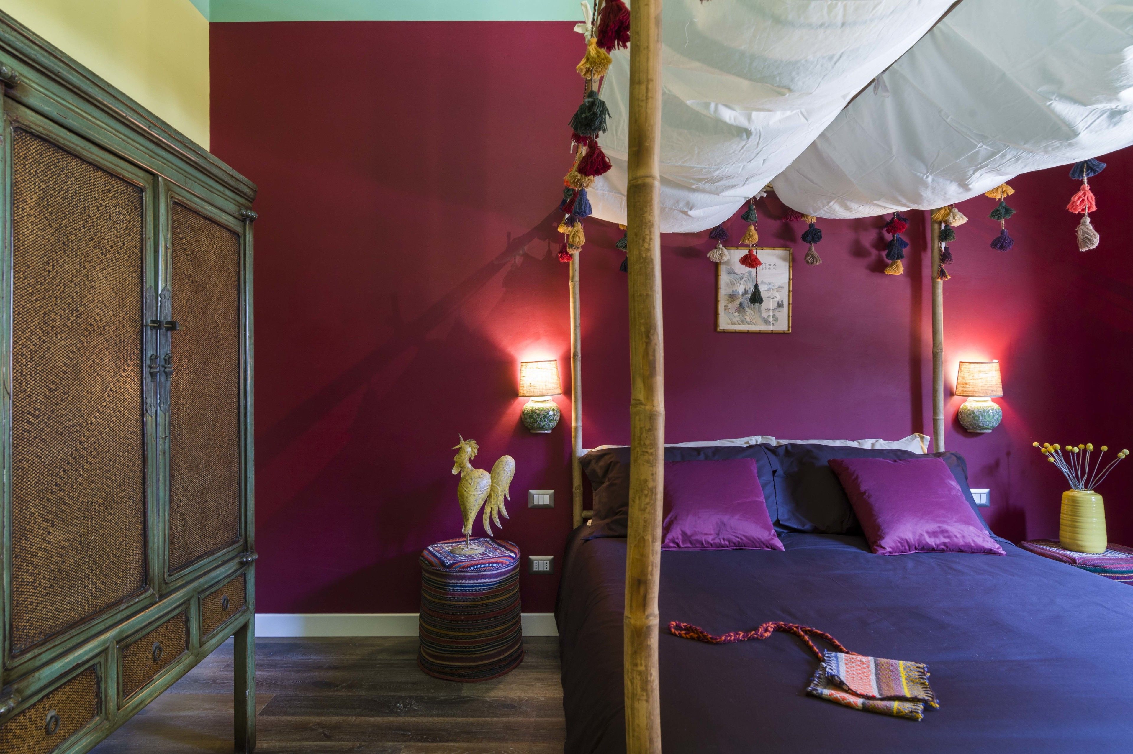 Une chambre à coucher avec un lit à baldaquin, un mur d’accent rouge et un tabouret décoratif orné d’une figurine.