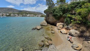 A rocky shoreline with clear water, a bench, and a view of a town in the background. - Villa Portomare (Markopoulo Mesogaias)
