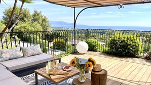 Eine Terrasse mit einer Sitzecke, einem Tisch mit Getränken und Speisen und Blick aufs Meer.