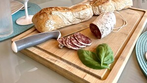 Eine Küche mit einem Holzbruchbrett, einem Brotlaib, geschnittenem Salami und einem grünen Blatt auf der Arbeitsfläche.