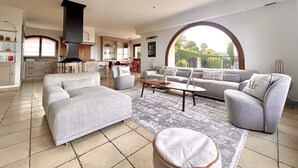 Ein geräumiges Wohnzimmer mit einem großen Sofa, einem Couchtisch und Blick auf die Küche sowie den Außenbereich durch ein großes Fenster.