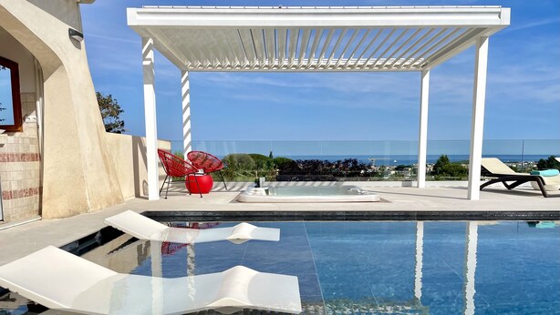 Ein moderner Poolbereich im Freien mit einer Pergola, Liegestühlen und Blick aufs Meer.