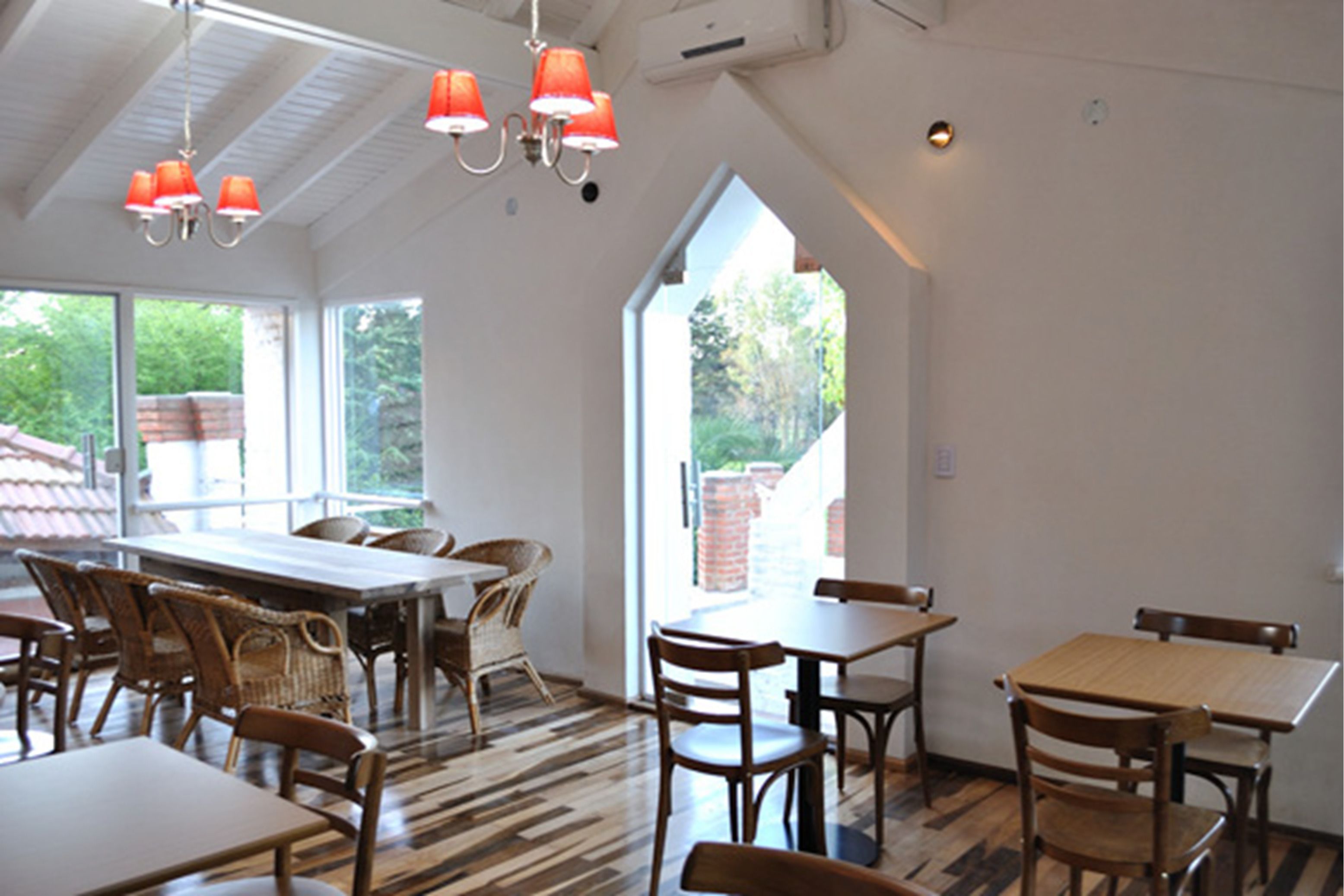 A dining area with high ceilings, large windows, and a mix of wooden and wicker furniture.