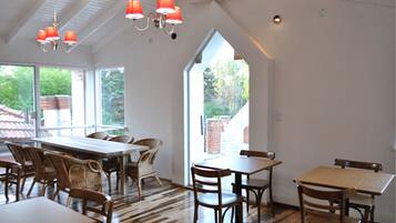 A dining area with high ceilings, large windows, and a mix of wooden and wicker furniture.