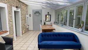 Une pièce baignée de lumière, avec un canapé bleu, une petite table ronde et un coin repas comprenant une table et des chaises en bois.