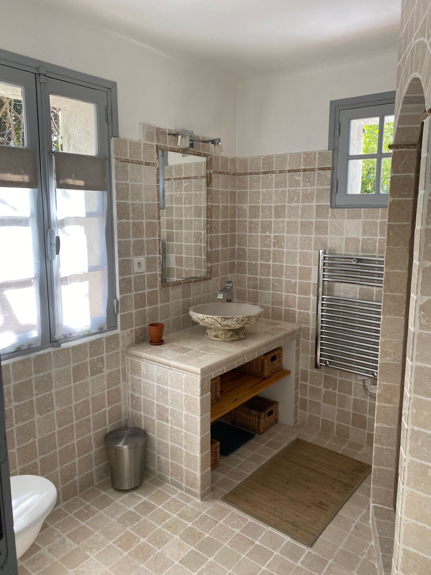 A bathroom with a tiled floor, a sink with a decorative basin, a mirror, a window, and a towel rack.